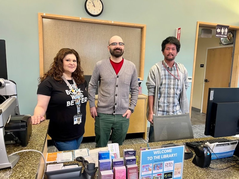 three people stand at library front desk