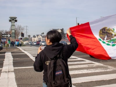 A young woman holds a Mexican flag at a busy intersection