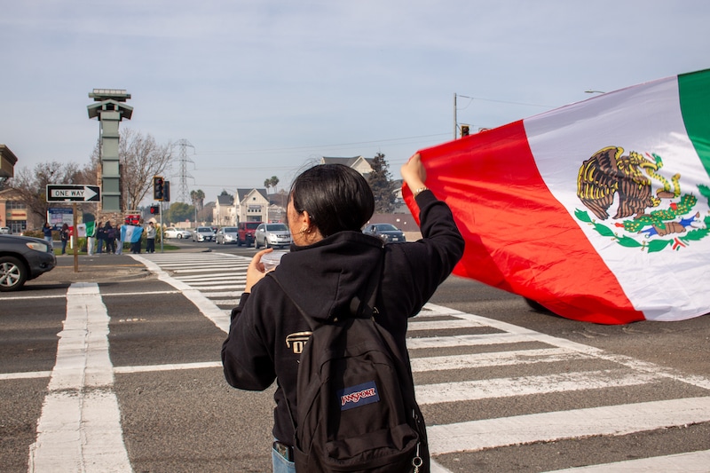 A young woman holds a Mexican flag at a busy intersection