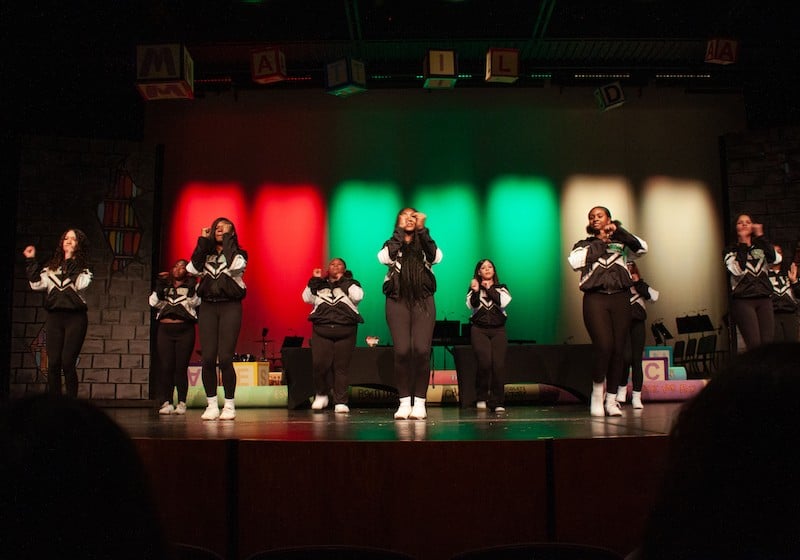Seven members of the cheer team dancing on a stage in front of red black and green lit panels