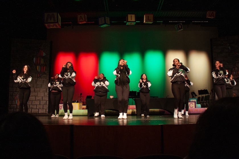Seven members of the cheer team dancing on a stage in front of red black and green lit panels