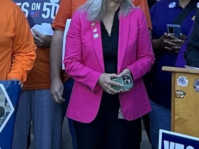 woman standing in pink blazer surrounded by Yes on 50 advocates