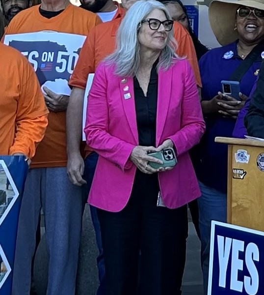 woman standing in pink blazer surrounded by Yes on 50 advocates