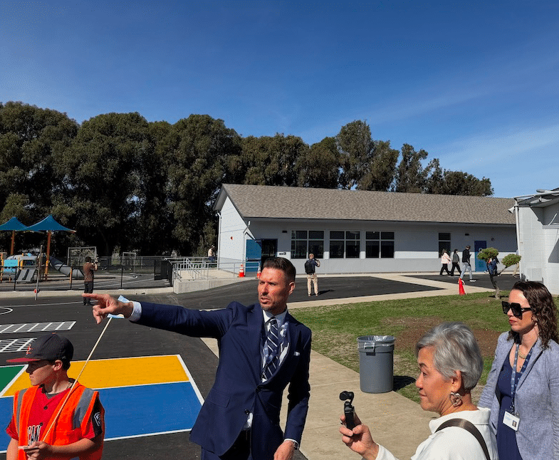 man pointing in front of a school while people look