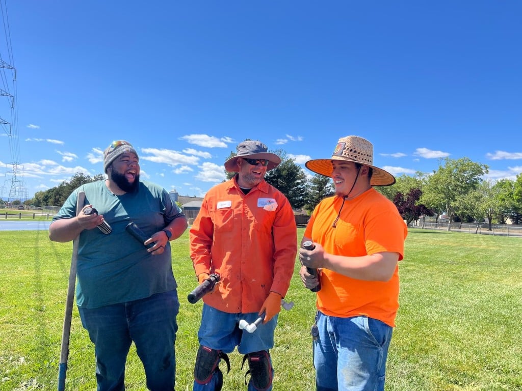 three men standing talking in park with tools