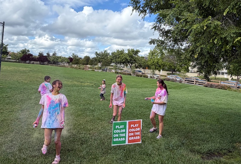 four girls and a child running around a lawn covered in colors