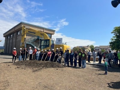 group of people standing with shovels for a photo op on a pile of dirt in front of a bulldozer