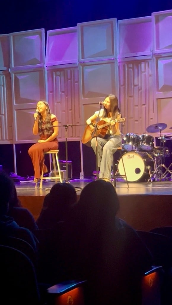 two girls sitting and singing on a stage