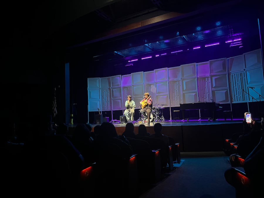 two boys sitting and singing on a stage