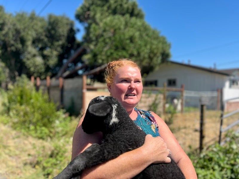 woman holding a black lamb in her arms in front of home