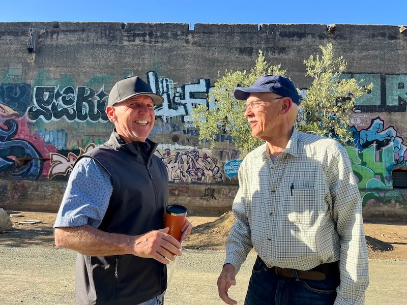 two men talking and smiling in front of graffiti covered concrete